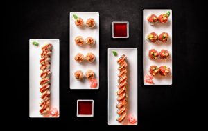 Four plates of sushi and sauce on a dark background